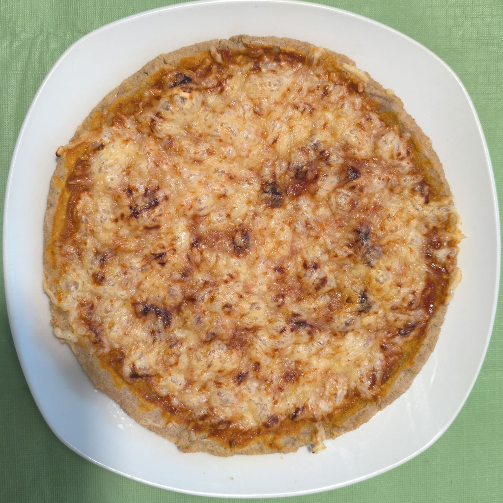 Draufsicht auf eine ganze, rund gebackene Pizza auf einem weißen Teller. Der glutenfreie Boden aus der Bio-Backmischung broat 'das Dünne' ist goldbraun gebacken und mit Tomatensoße und geschmolzenem Käse belegt