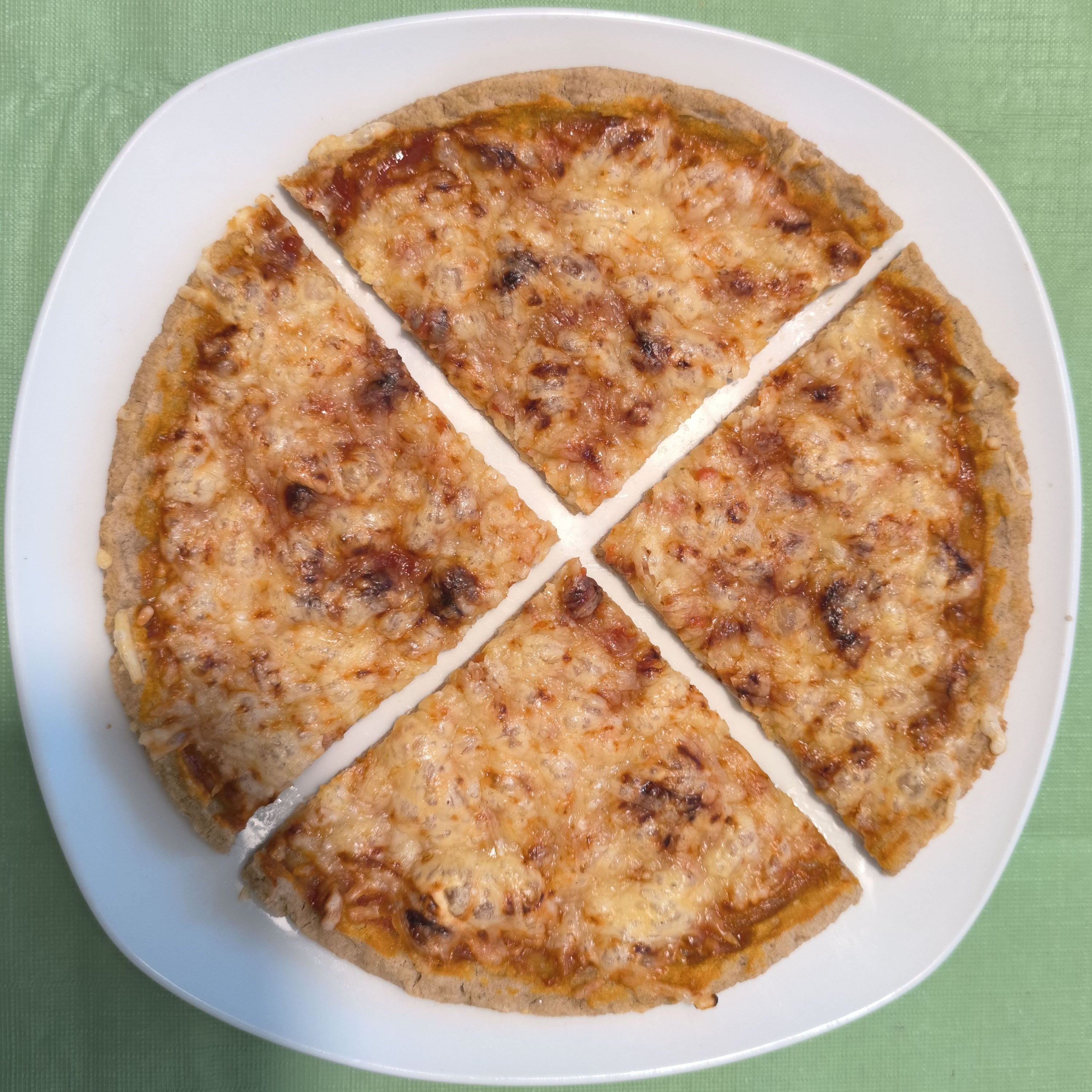 Draufsicht auf eine in vier Stücke geschnittene glutenfreie Pizza auf einem weißen Teller. Der Boden der Backmischung broat 'das Dünne' wirkt stabil und knusprig, belegt mit Käse und Tomatensoße.