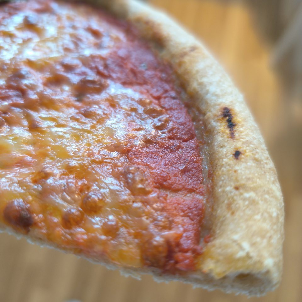 Nahaufnahme eines Stücks gebackener glutenfreier Pizza aus der broat® Bio-Backmischung Pizza. Glutenfreie Pizza. mit Hefe