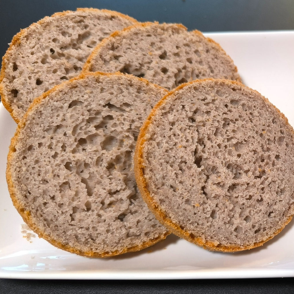 Vier Scheiben des fertig gebackenen noOat Brotes Sorte das Feine auf einem weißen Teller. Das glutenfreie Brot zeigt eine lockere, poröse Krume und eine hellbraune Kruste, hergestellt ohne Zusatzstoffe."